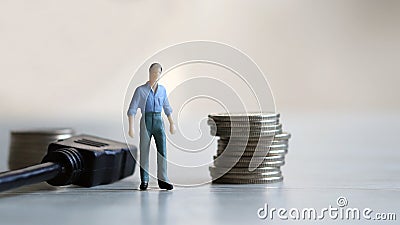 Business concept about work and wages. MiniatureÂ manÂ standingÂ betweenÂ aÂ cableÂ lineÂ andÂ aÂ pileÂ ofÂ coin. Stock Photo